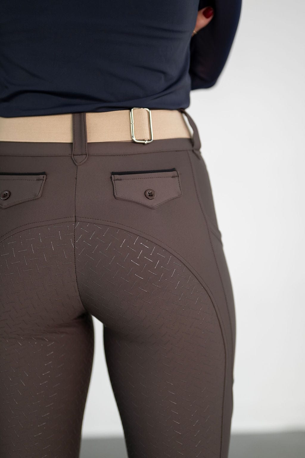 girl standing next to chair wearing the white cassidy top and earth brown lux zip breeches